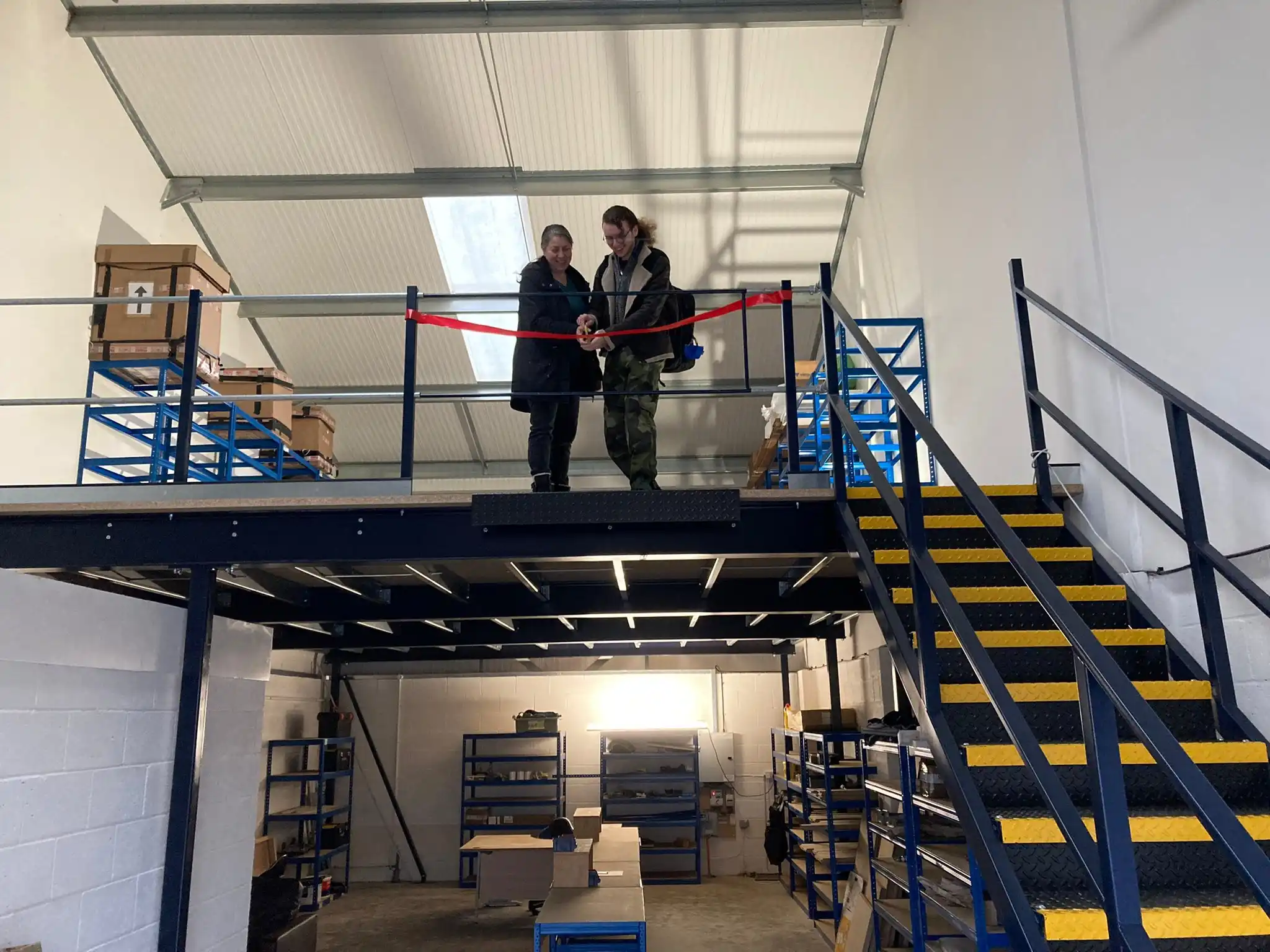 Jacob and Therese cutting a red ribbon on the top of the factory opening the factory